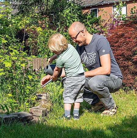 Hier staat een foto met vader en kind die plantjes water geven